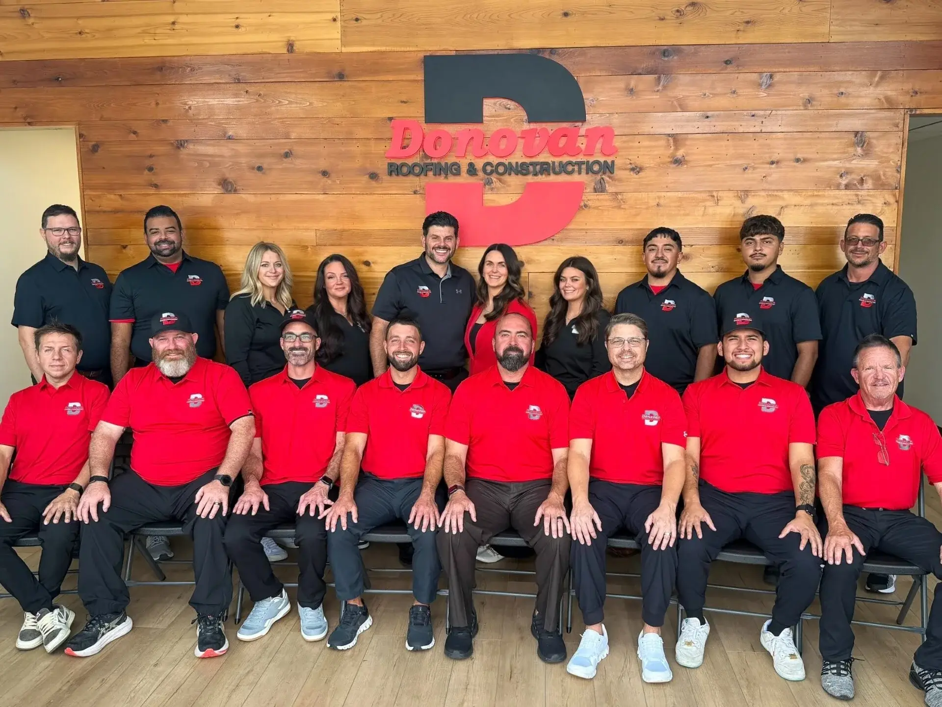 The Donovan Roofing & Construction team in front of the company logo wall