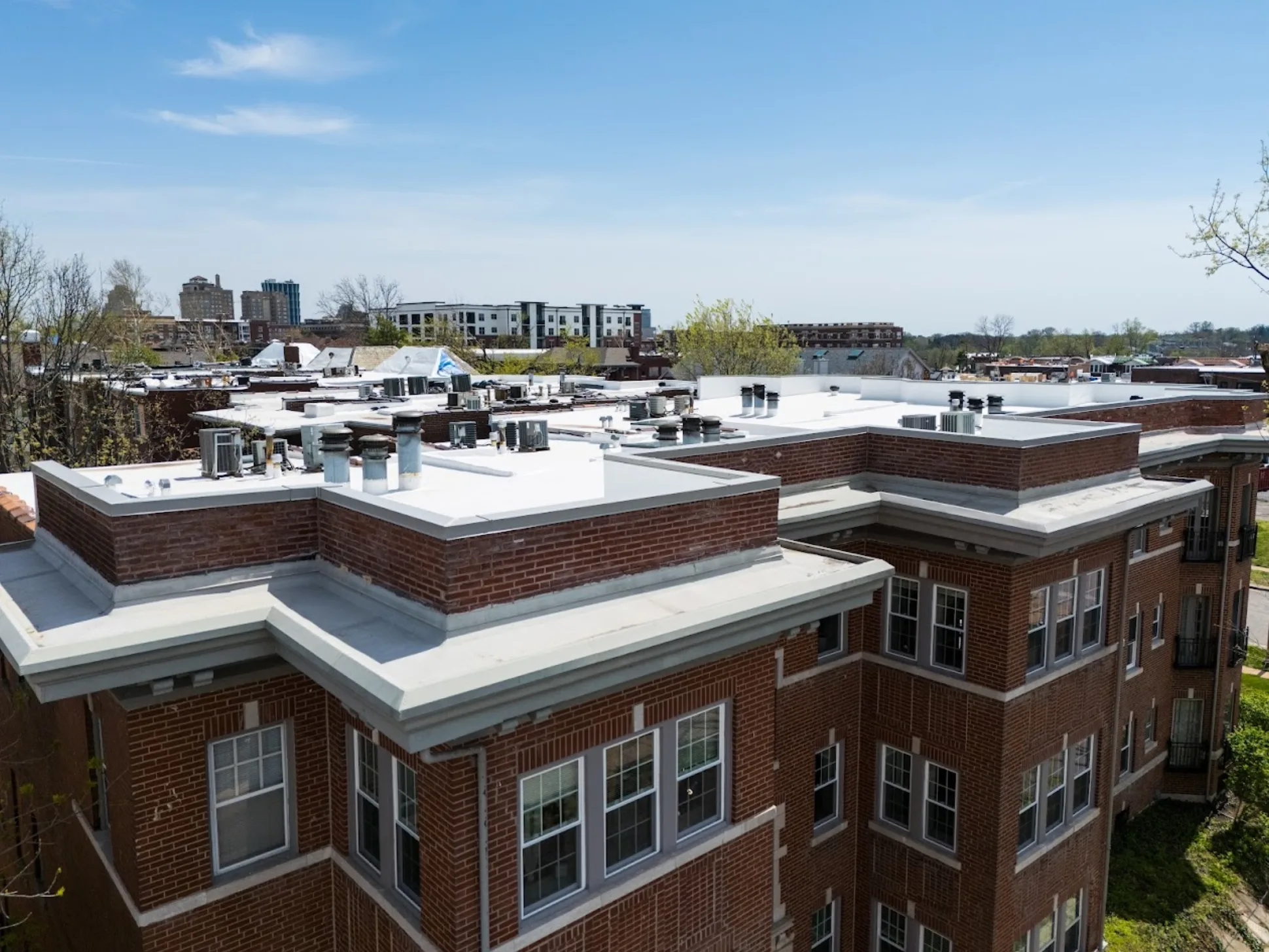 Corner aerial of a brick apartment building with a finished white flat roof and bay windows