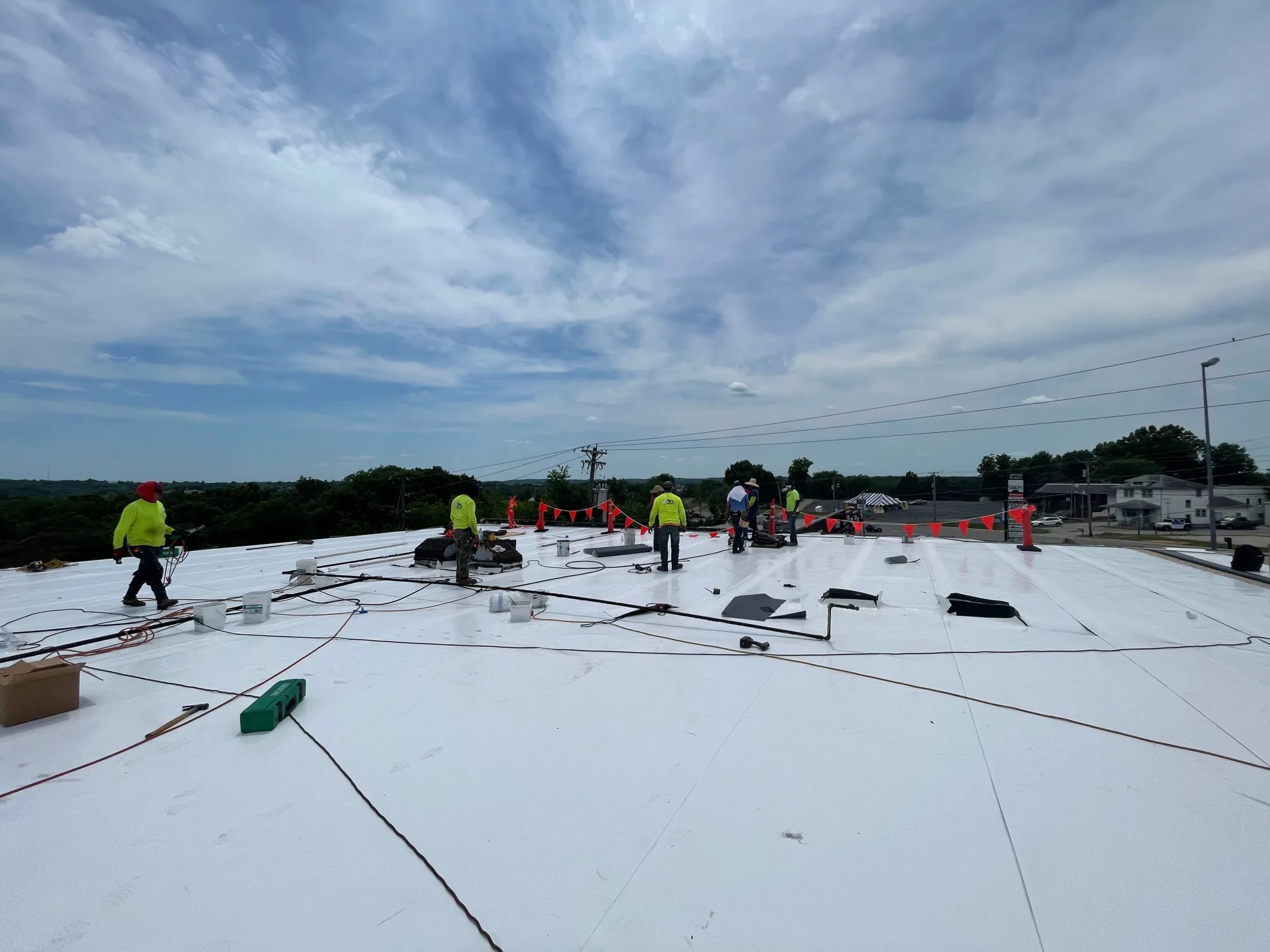 Crew installing a white TPO membrane across a large commercial flat roof