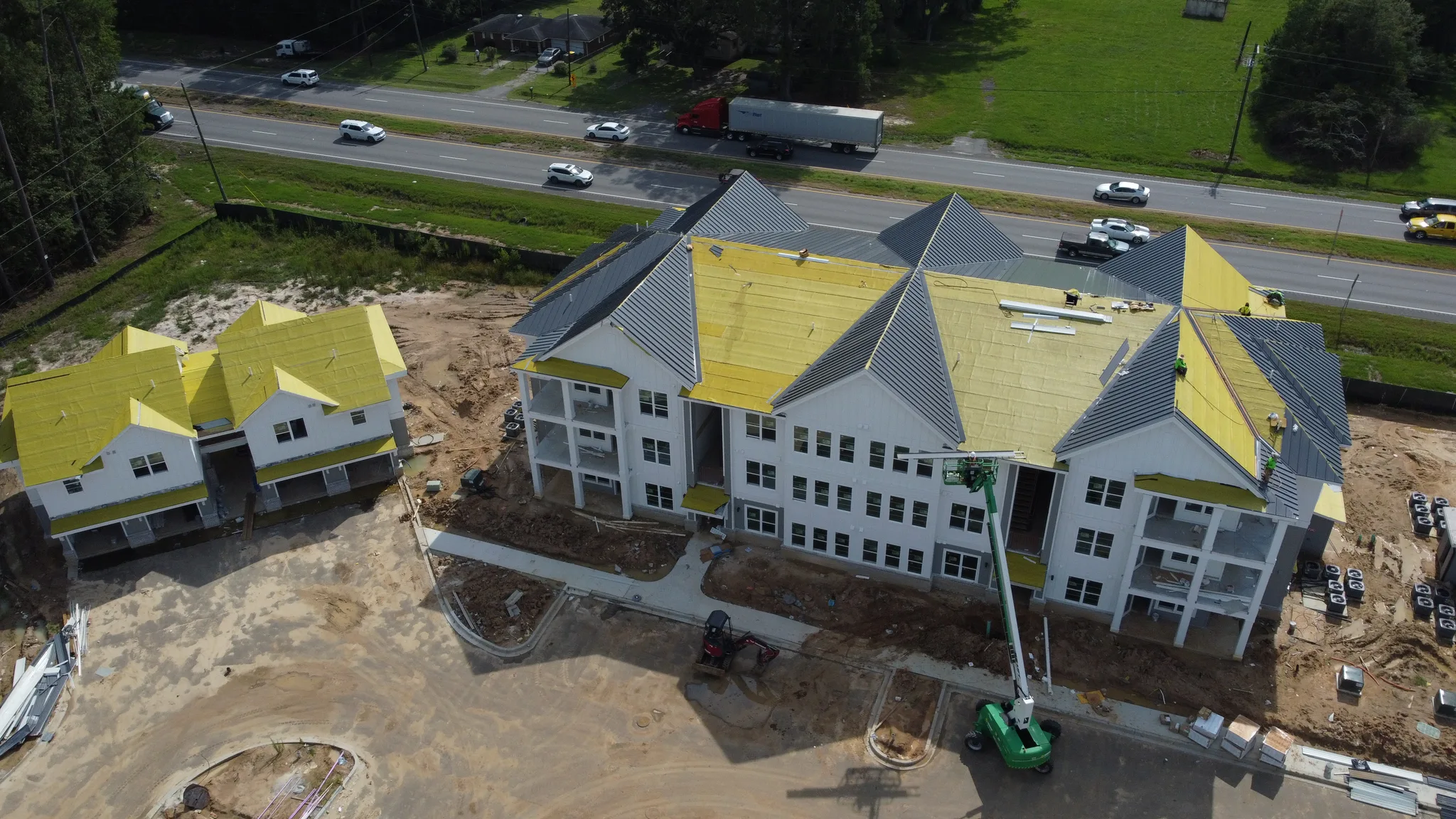 Aerial of a large commercial building mid-install with gray standing seam metal panels going on