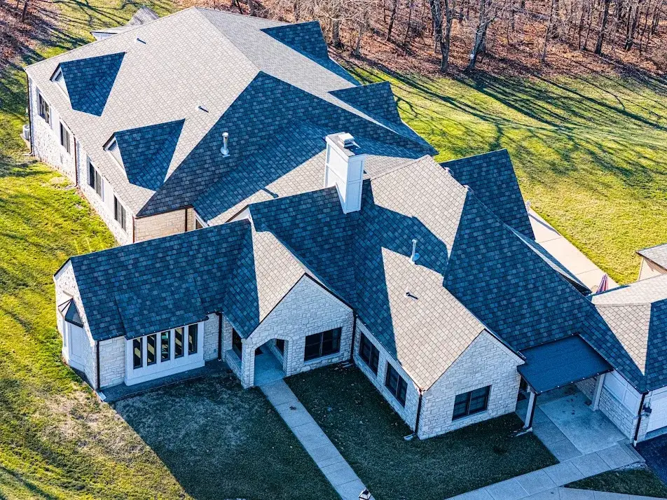 Aerial of a large stone home with a multi-pitched charcoal designer shingle roof