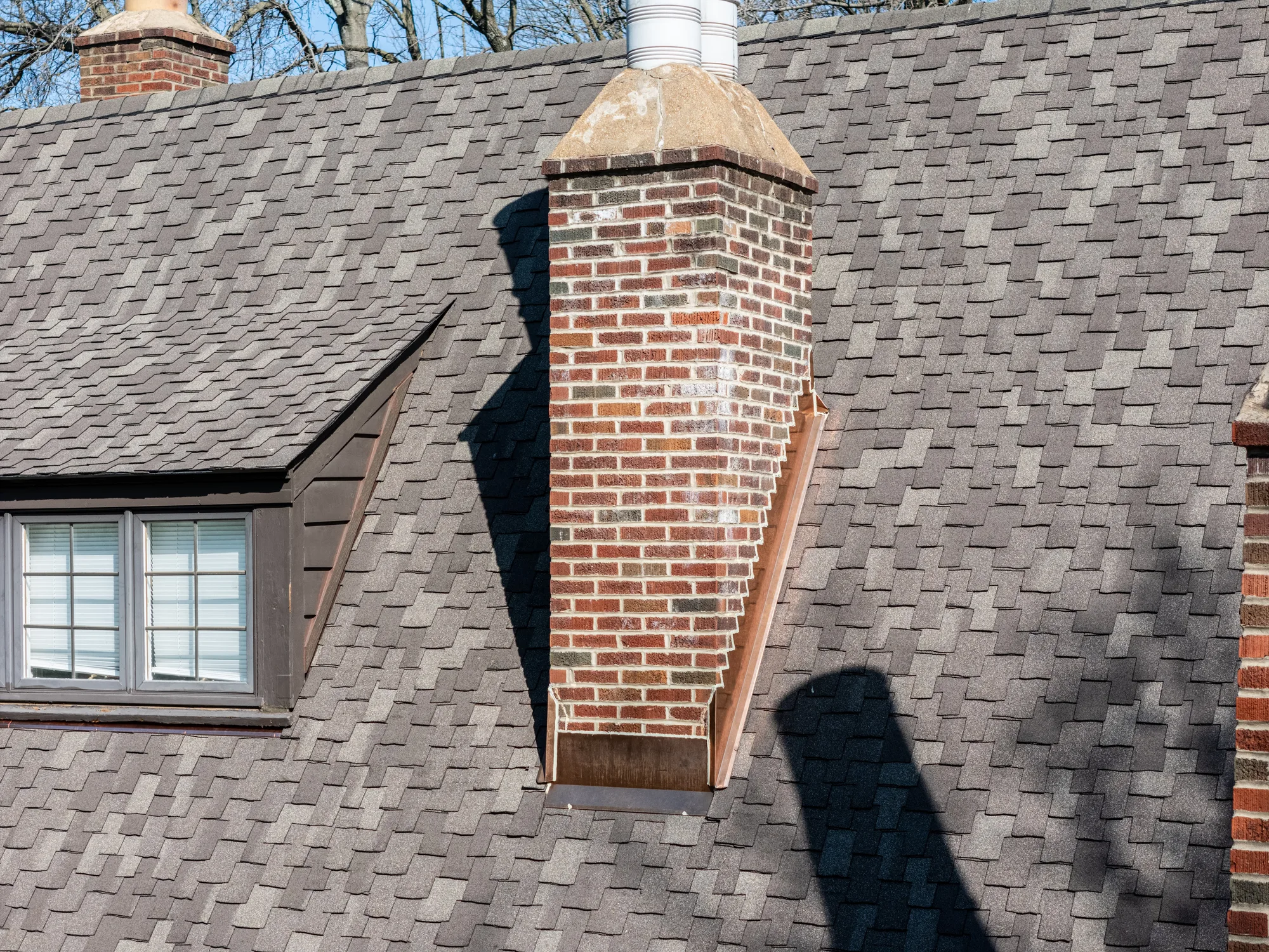 Dimensional shingle field meeting a brick chimney on a Clayton Tudor