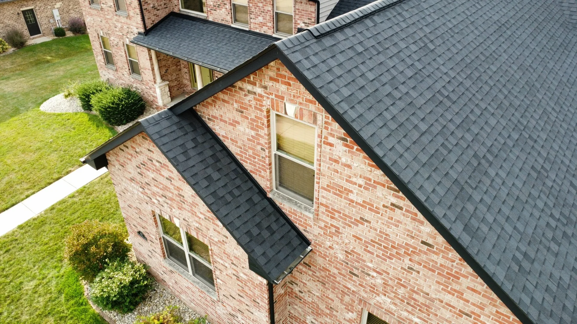 Charcoal architectural shingle roof over a brick home, close aerial view