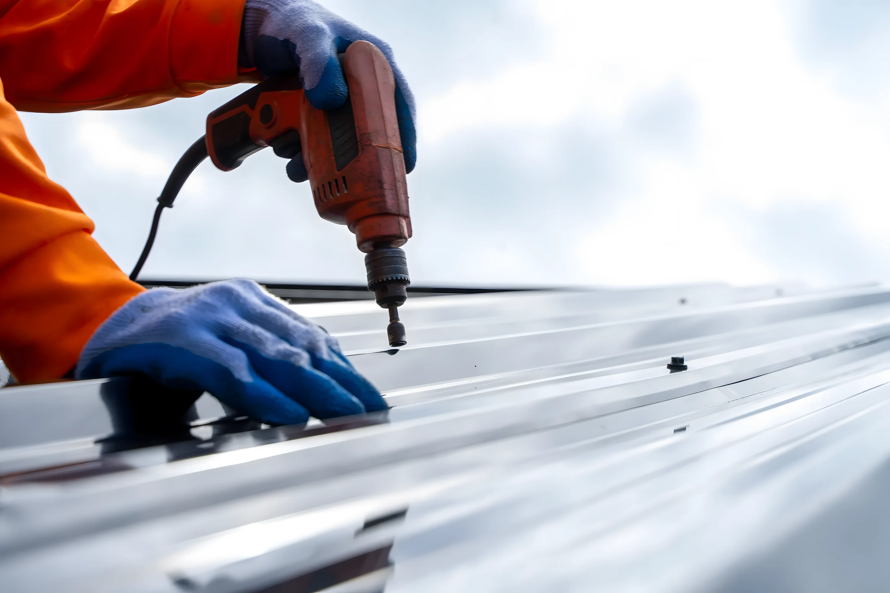 Gloved hands inspecting a roof with a cordless drill